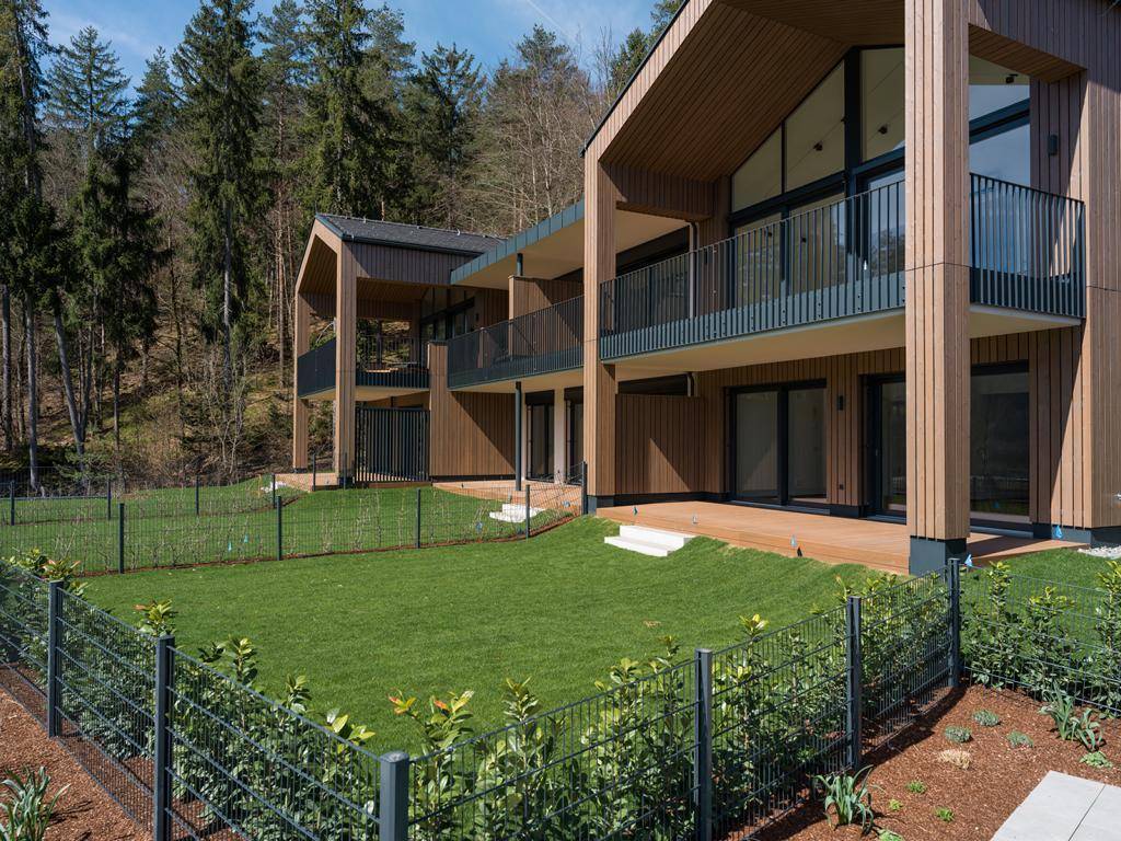 Moderne Reihenhäuser mit Holzfassade, Balkonen und privaten Gärten am Waldrand.