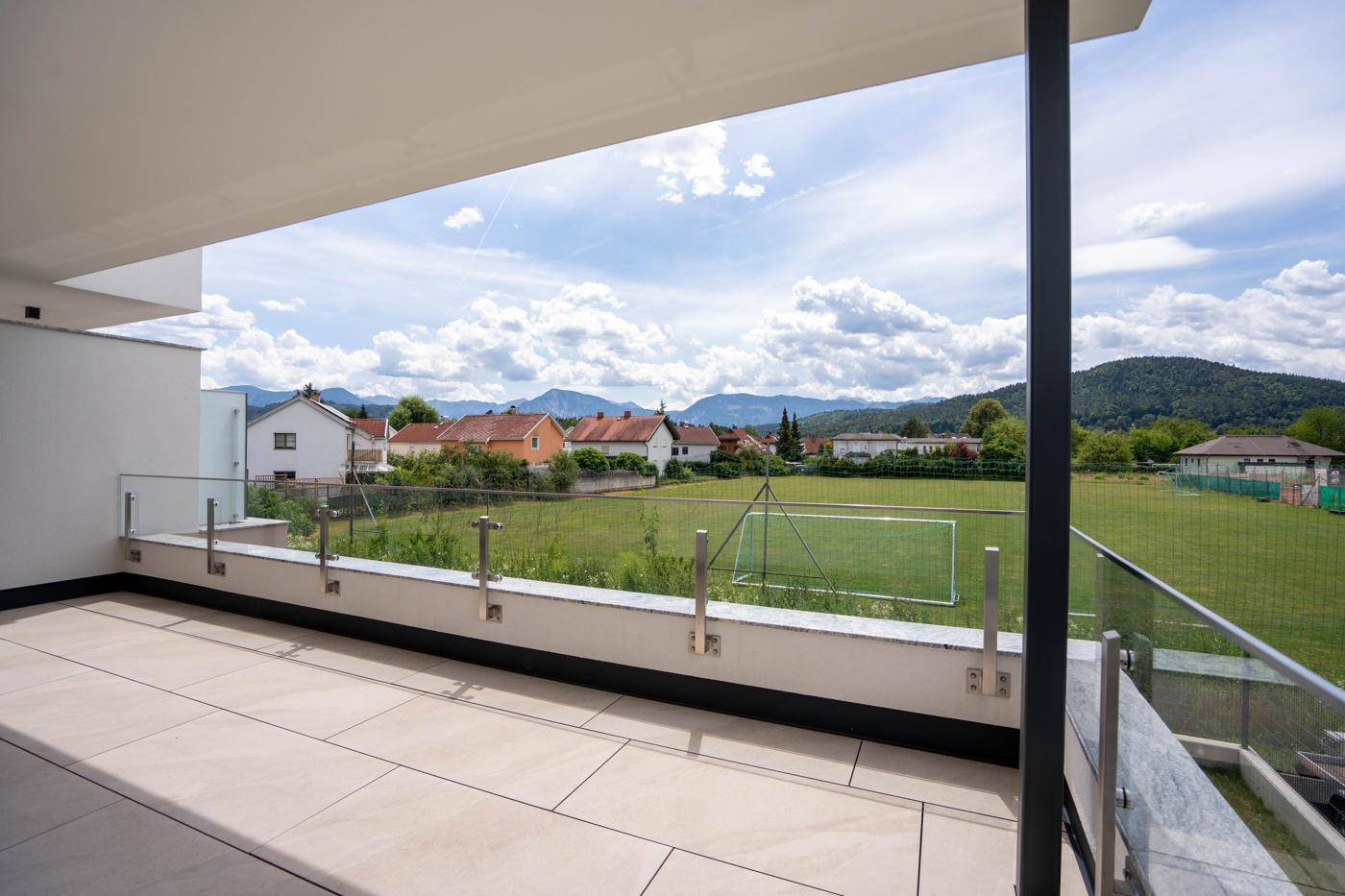 Geräumiger Balkon mit Fliesenboden und Glasgeländer, bietet einen weiten Blick auf die Berge und grüne Felder.