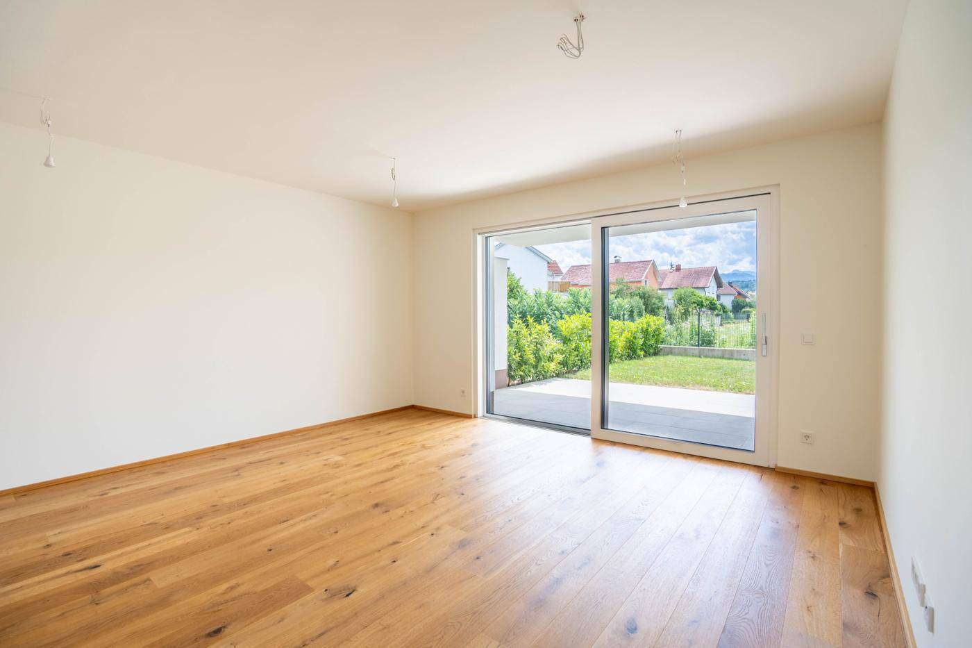 Geräumiger, heller Raum mit Holzboden und großen Fenstern, die den Blick in den Garten freigeben.