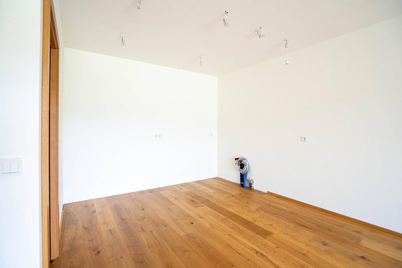 Leerer Raum mit hellem Holzboden und weiß gestrichenen Wänden, bereit für die individuelle Gestaltung.