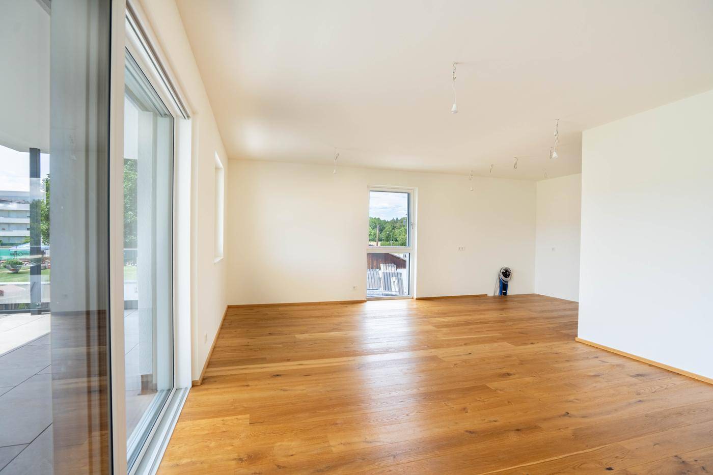 Heller, leerer Raum mit Holzboden und großen Fenstern, die viel Tageslicht hereinlassen.