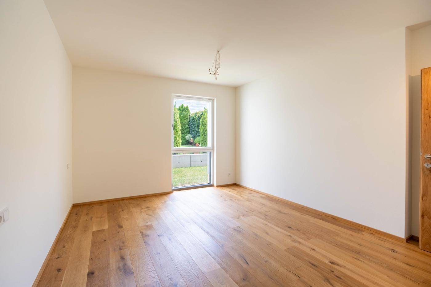 Helles Schlafzimmer mit Holzboden und einem Fenster, das einen Blick ins Grüne ermöglicht.