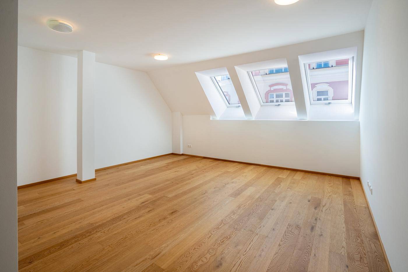 Geräumiger, unmöblierter Raum mit Holzboden und schrägen Dachfenstern, ideal für individuelle Gestaltung.