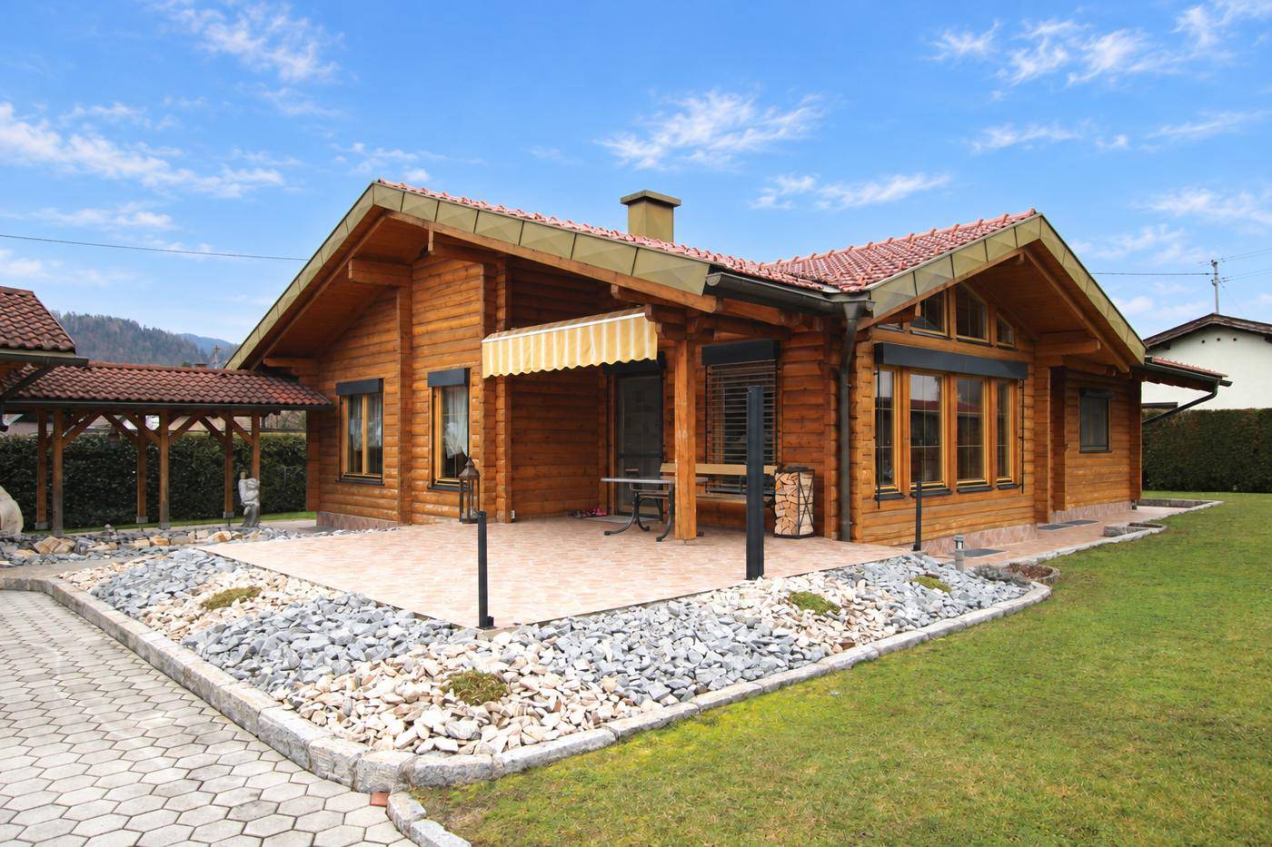 Gemütliche Terrasse am Blockhaus mit Markise, Sitzgelegenheiten und Kiesbeet.