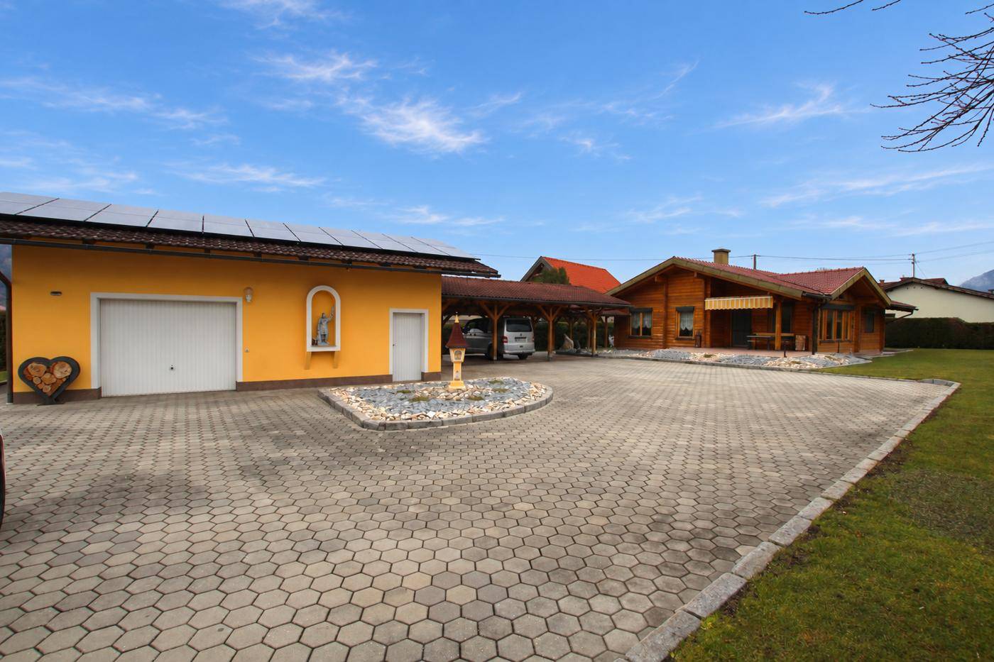 Gesamtansicht des Anwesens mit Blockhaus, separater Garage und großem gepflasterten Vorplatz.