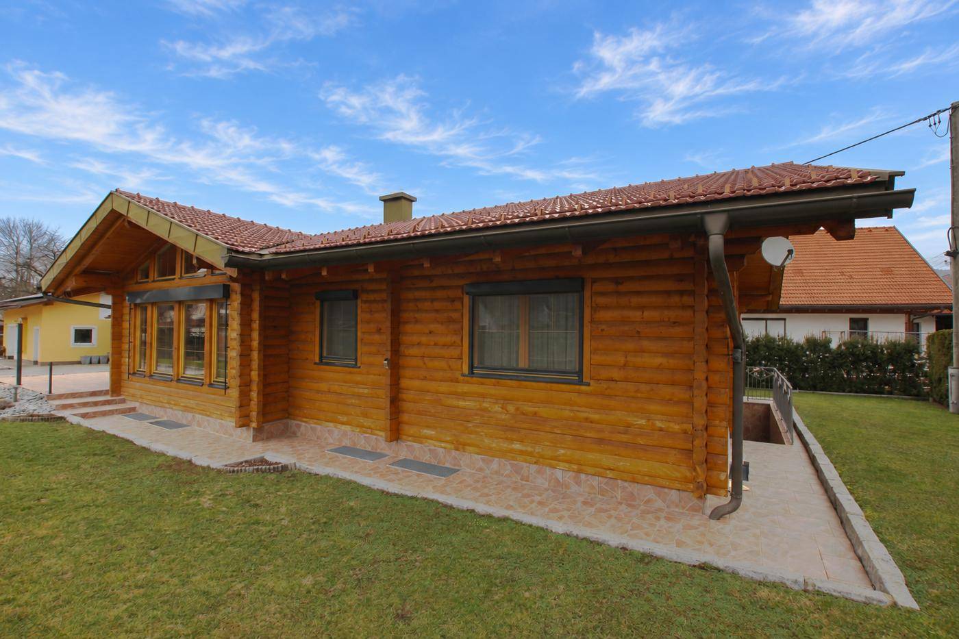 Seitenansicht des Holzhauses mit Zugang zum Keller und umlaufendem Rasenbereich.