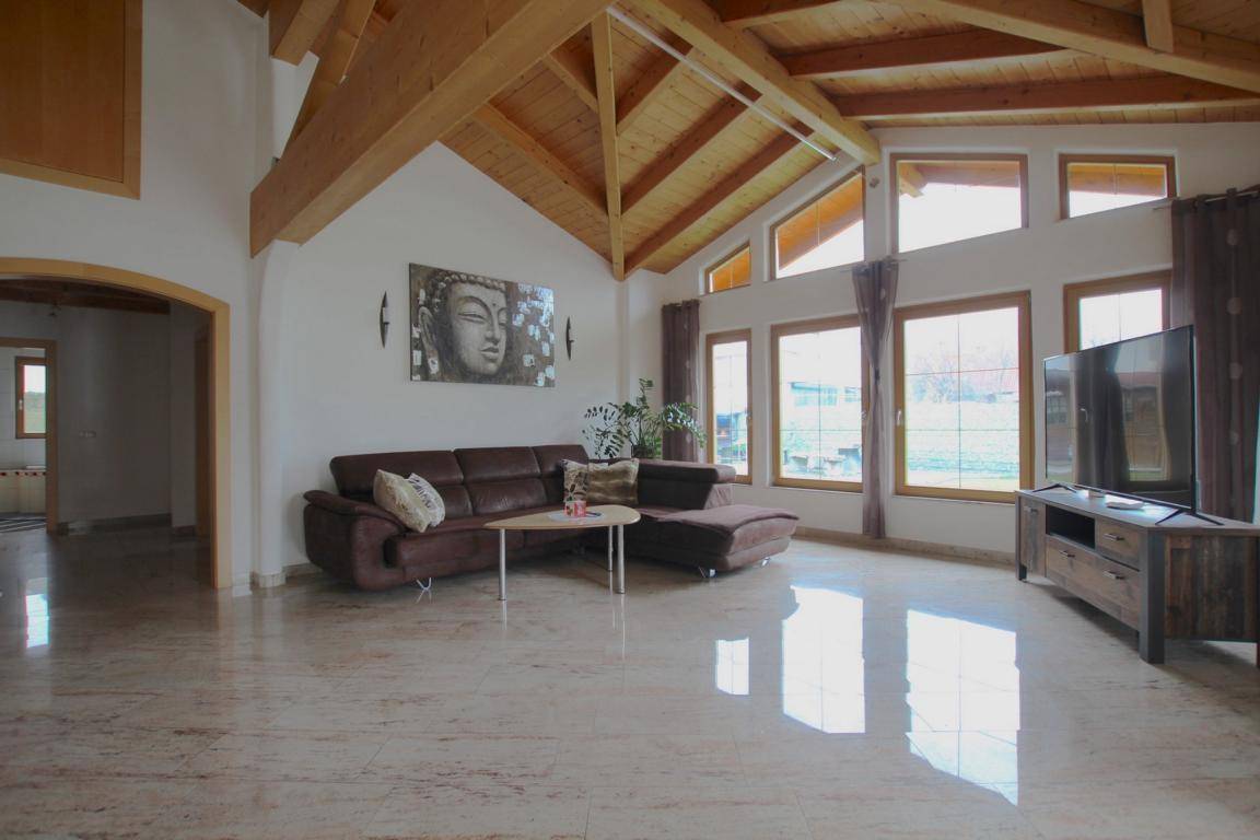 Helles Wohnzimmer mit hohen Holzdecken, großen Fenstern und glänzendem Marmorboden.