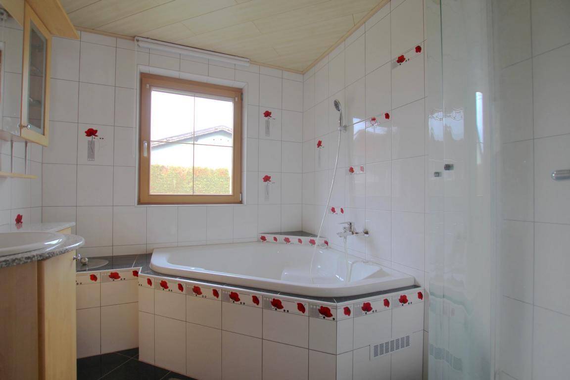 Badezimmer mit Eckbadewanne, Dusche und weißen Fliesen mit roten Akzenten.