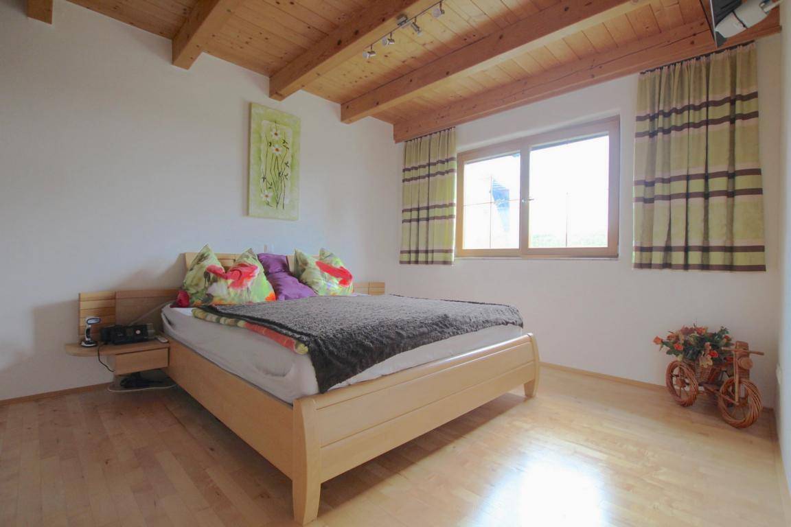 Helles Schlafzimmer mit Holzbalkendecke, Doppelbett und Blick ins Grüne.