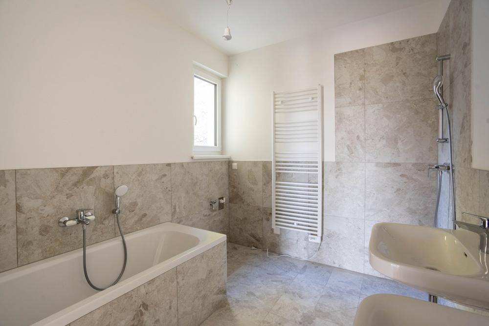 Modernes Badezimmer mit Badewanne, Waschbecken, beheiztem Handtuchhalter und Fenster.