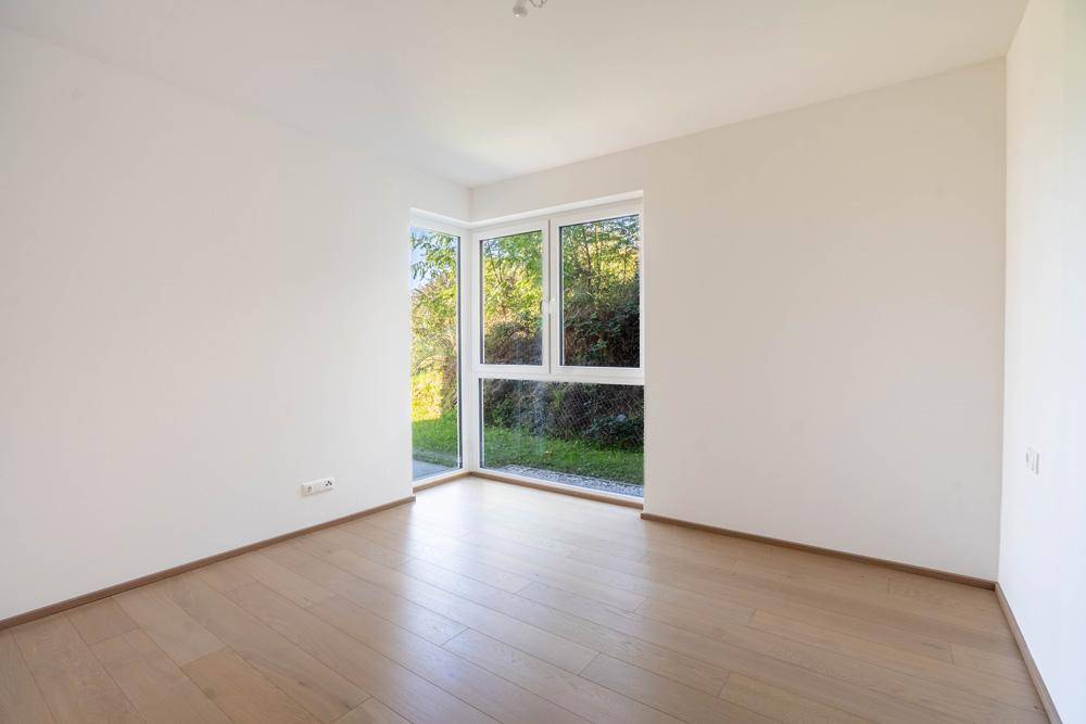 Helles Schlafzimmer mit Eckfenster und Blick ins Grüne, ausgestattet mit Holzfußboden.