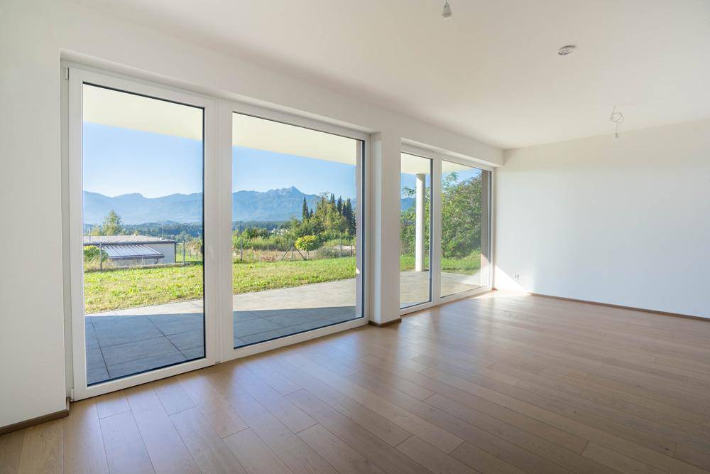 Lichtdurchfluteter Wohnraum mit großen Fenstern, Holzboden und weitem Blick auf die Landschaft.