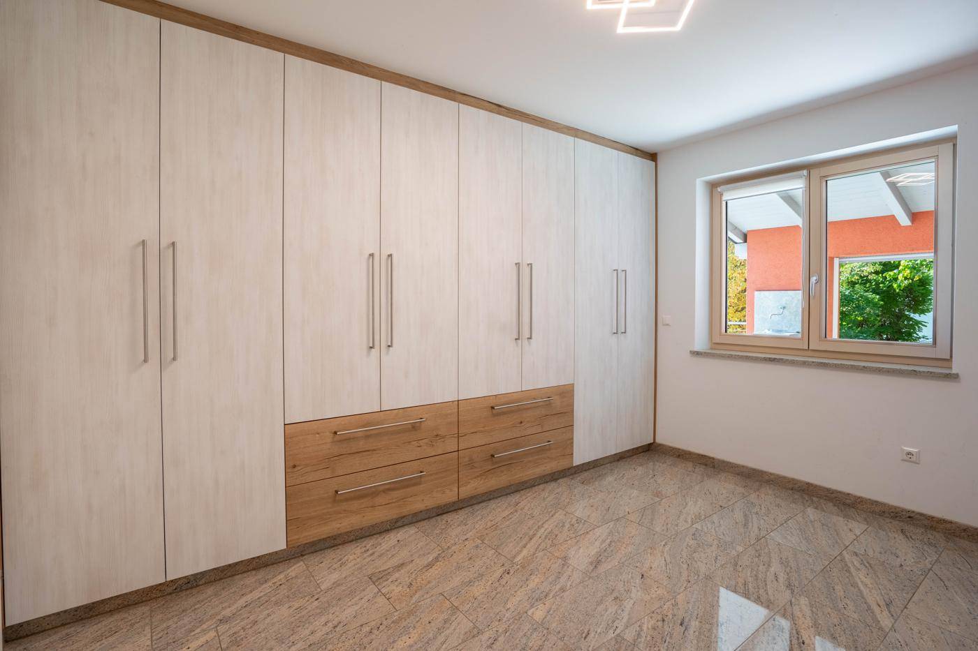 Schlafzimmer mit großem Einbauschrank in Holzoptik und Fliesenboden, hell und funktional gestaltet.