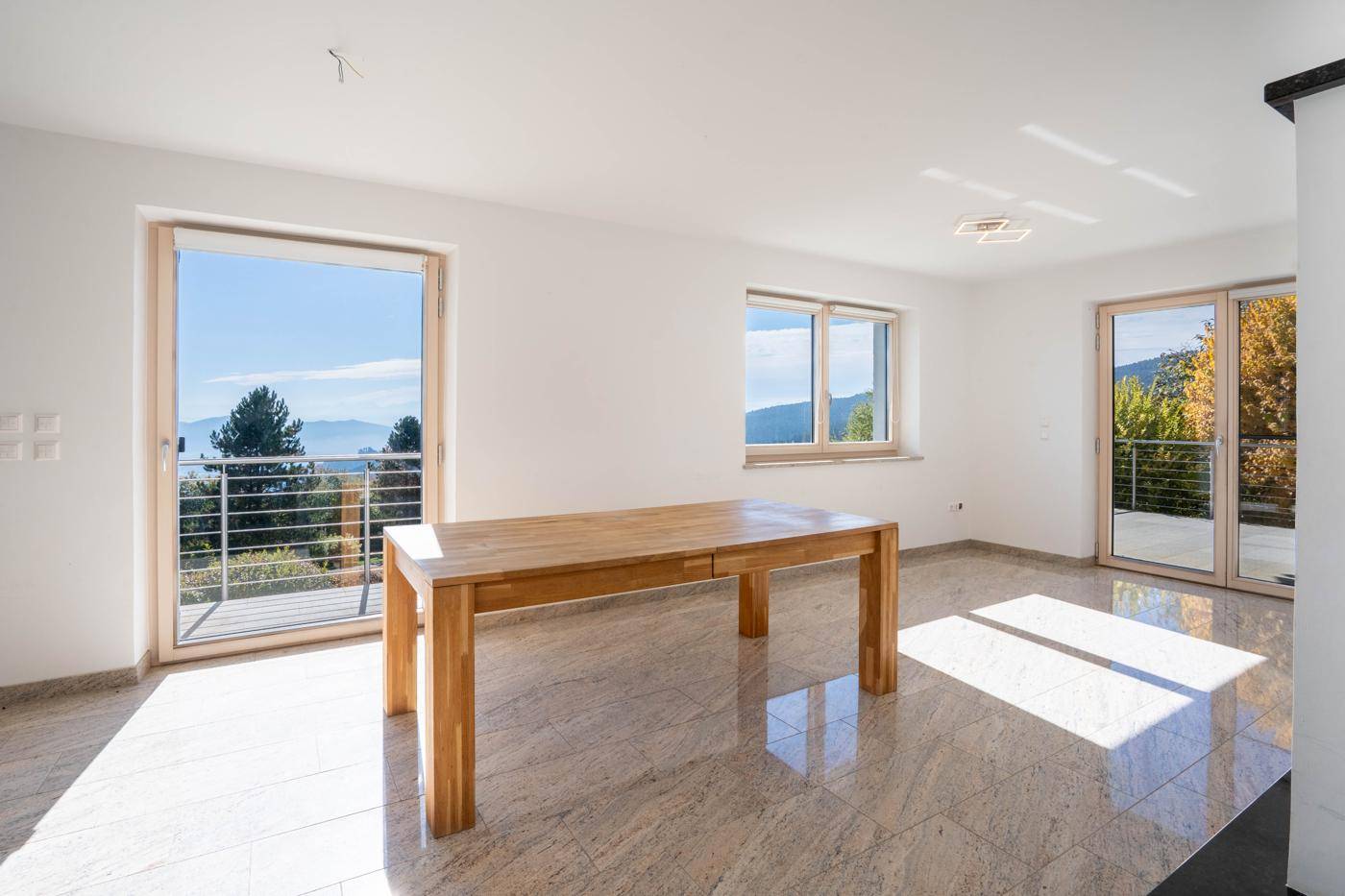Heller Wohn- und Essbereich mit Fliesenboden, Holztisch und Zugang zum Balkon mit Bergblick.