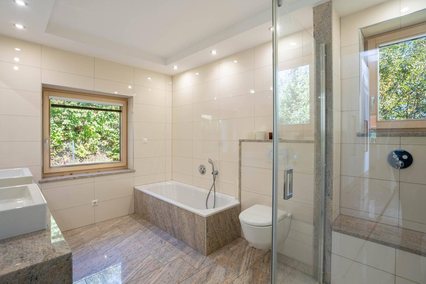 Modernes Badezimmer mit hellen Fliesen, Badewanne, begehbarer Dusche und Doppelwaschbecken.