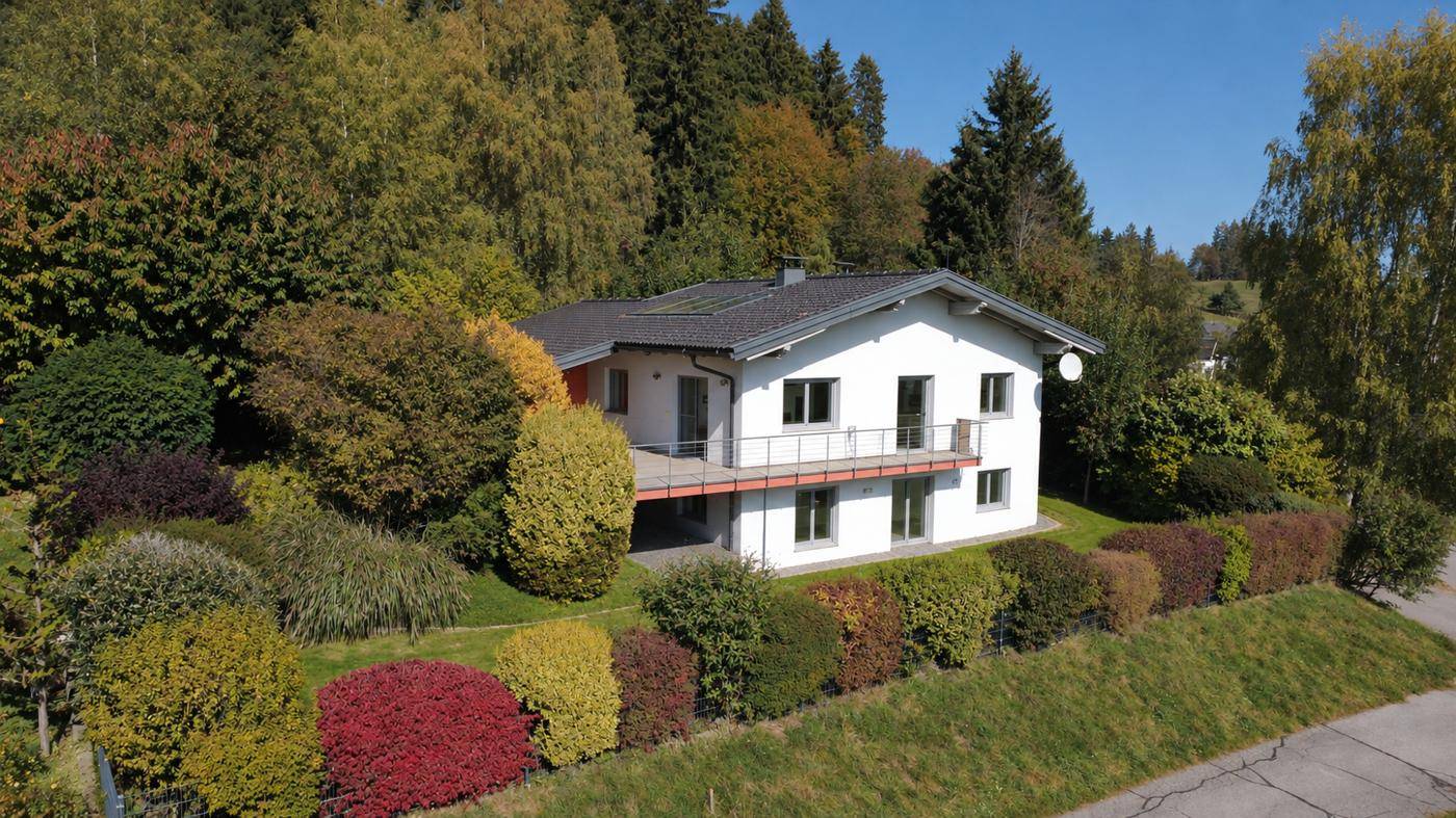 Modernes Einfamilienhaus mit weißer Fassade und großem Garten, eingebettet in eine grüne Hügellandschaft.