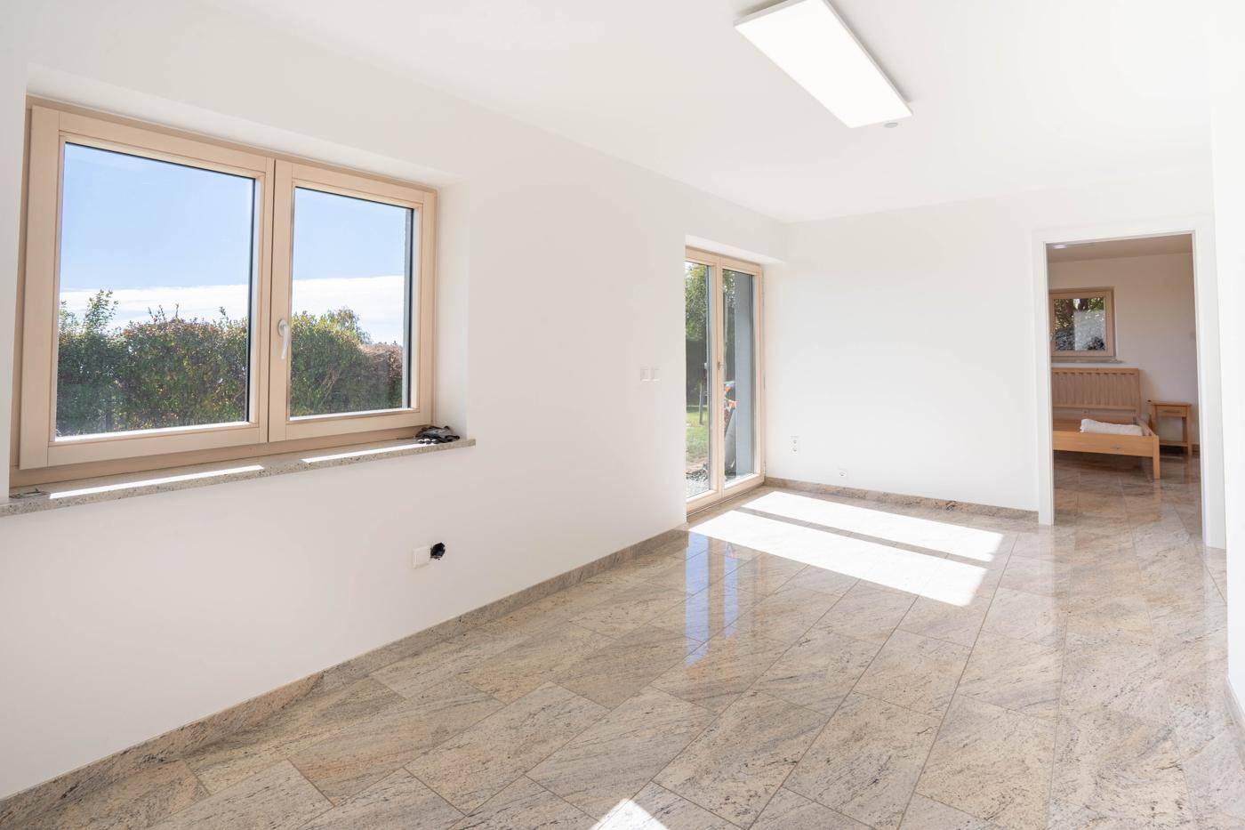 Heller Raum mit Fliesenboden und Zugang zum Garten, angrenzend an ein weiteres Zimmer.