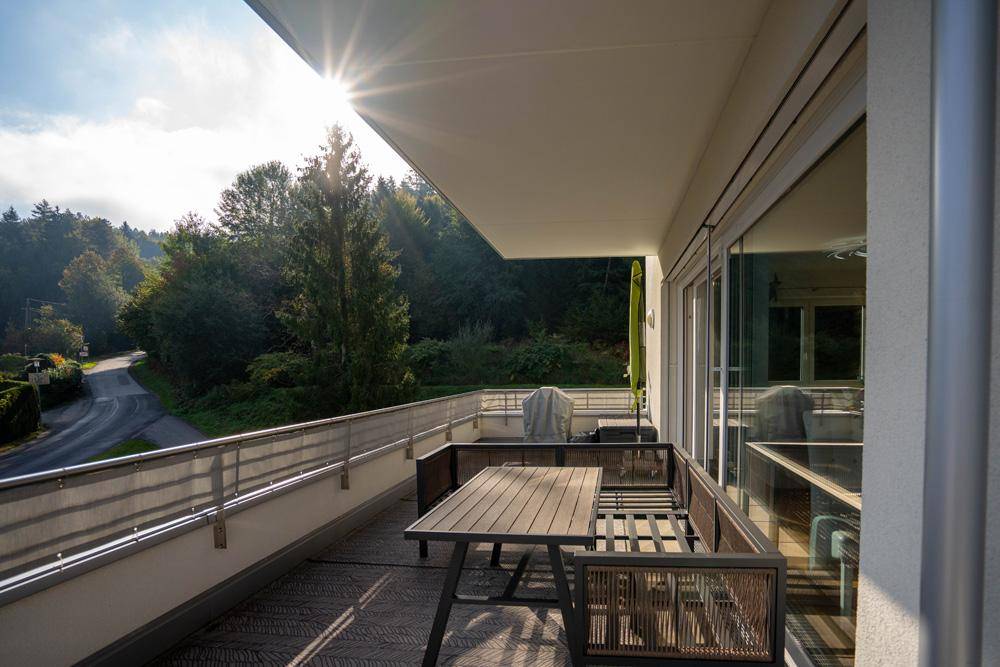 Sonniger Balkon mit Outdoor-Möbeln und Blick auf die umliegende Natur und Straße.