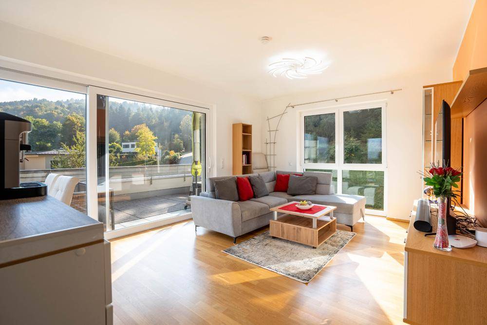 Gemütliches Wohnzimmer mit Ecksofa, Holzboden und großem Schiebefenster zum sonnigen Balkon.