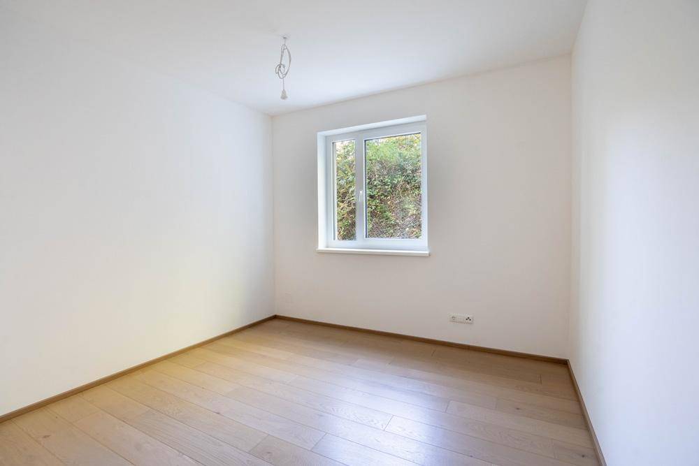 Ruhiges Zimmer mit Holzboden und Fenster, das einen Blick ins Grüne bietet.
