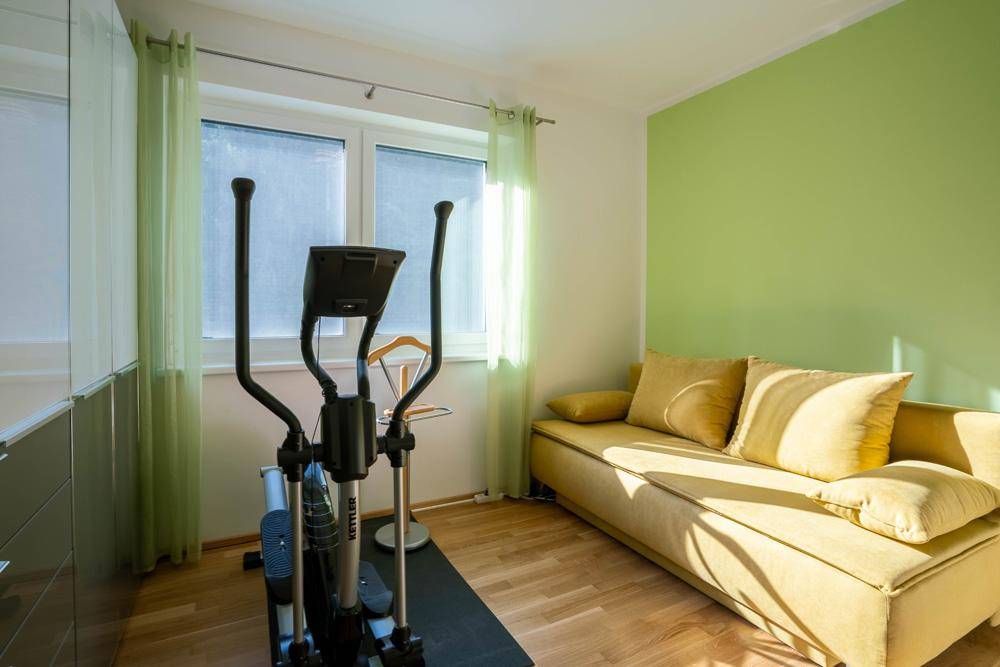 Flexibler Raum mit grün gestrichener Wand, Holzboden und Fenster, ideal als Büro oder Fitnessraum.