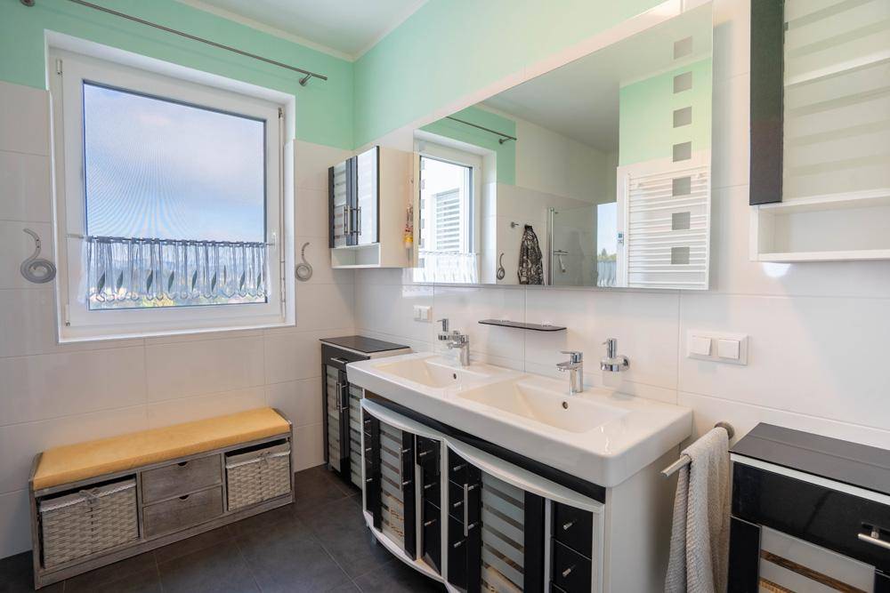 Modernes Badezimmer mit Doppelwaschbecken, großem Spiegel, Fenster und hellgrünen Akzenten.