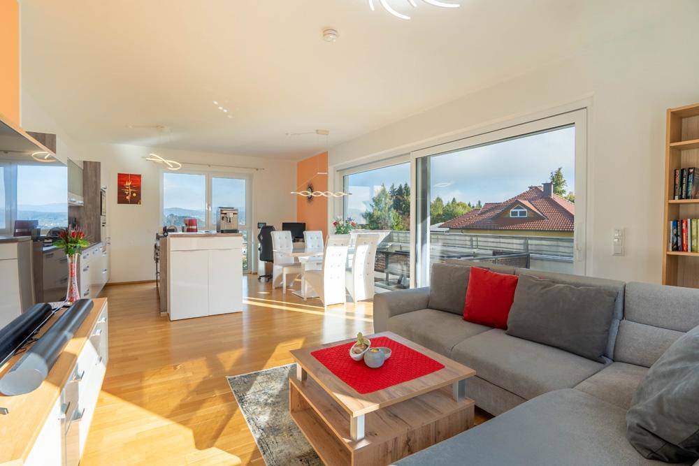 Helles, offenes Wohn-Esszimmer mit Holzboden, gemütlichem Sofa und Zugang zum Balkon.
