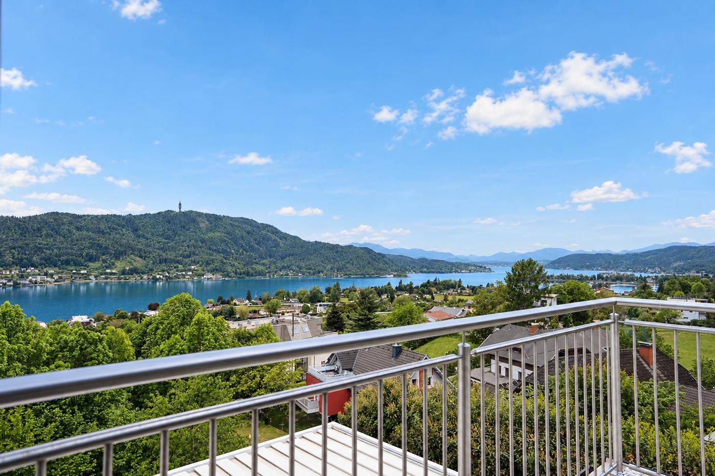Balkon mit Edelstahlgeländer und weitem Blick über den See, die Berge und die umliegende Landschaft.
