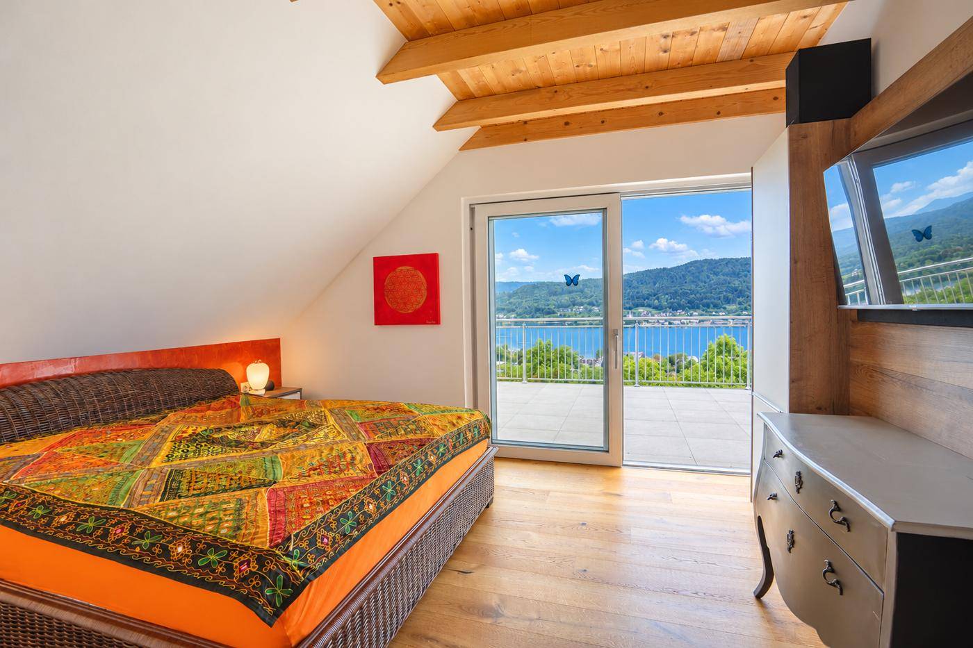 Gemütliches Schlafzimmer mit Holzboden, Zugang zur Terrasse und weitem Blick auf den See und die Berge.