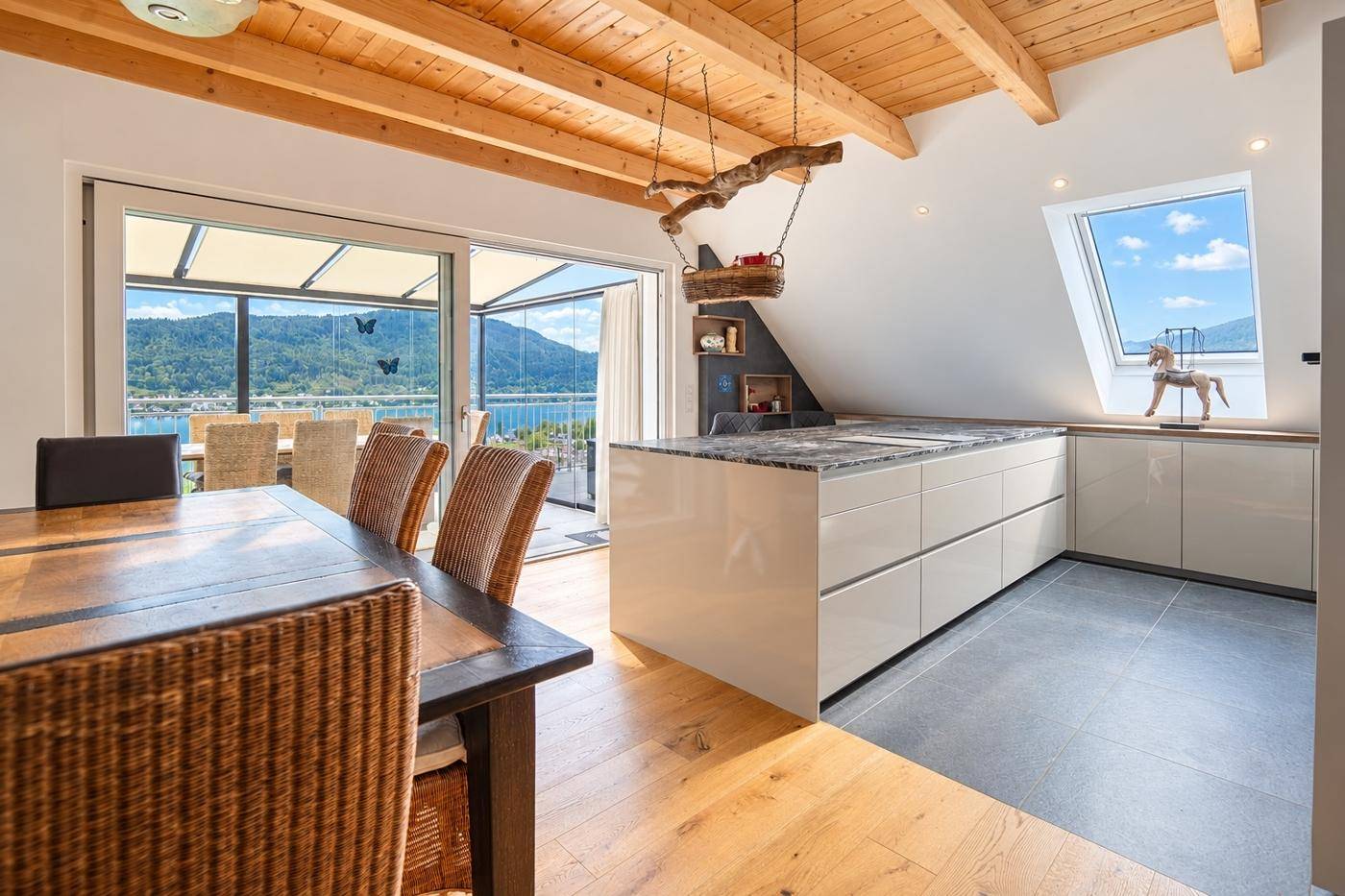Moderne Küche mit Kochinsel und Essbereich, offen zur Terrasse mit herrlichem See- und Bergblick.