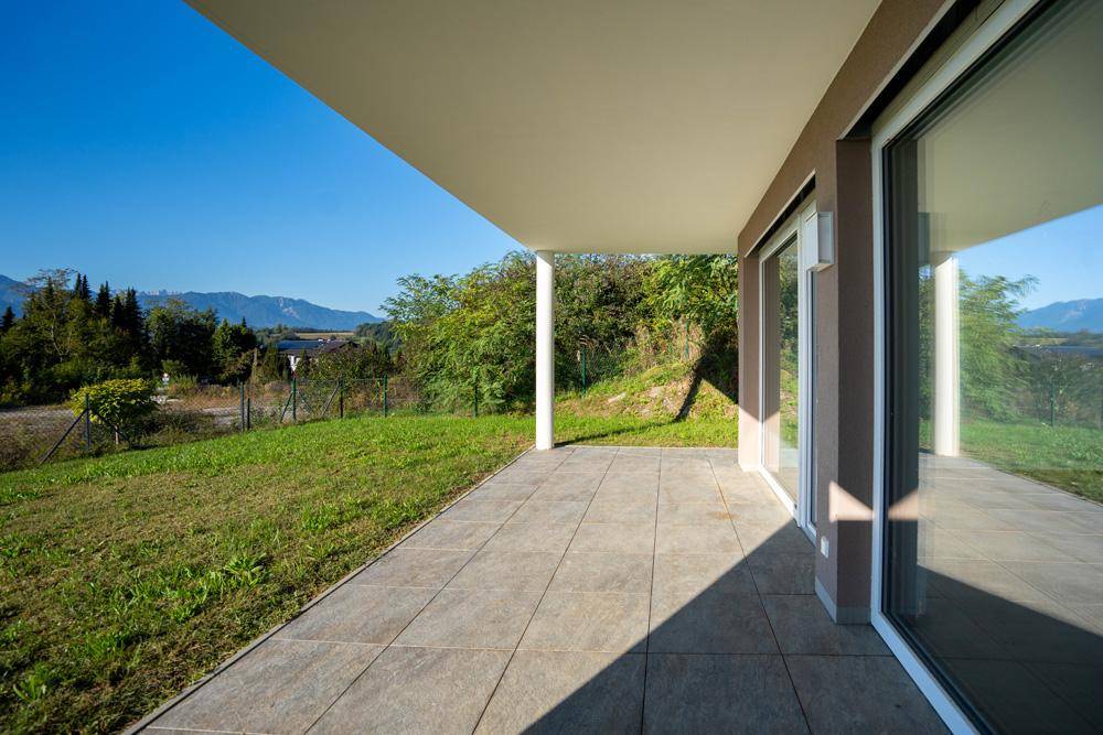 Überdachte Terrasse mit großformatigen Fliesen und Zugang zu den Innenräumen, mit Bergblick.