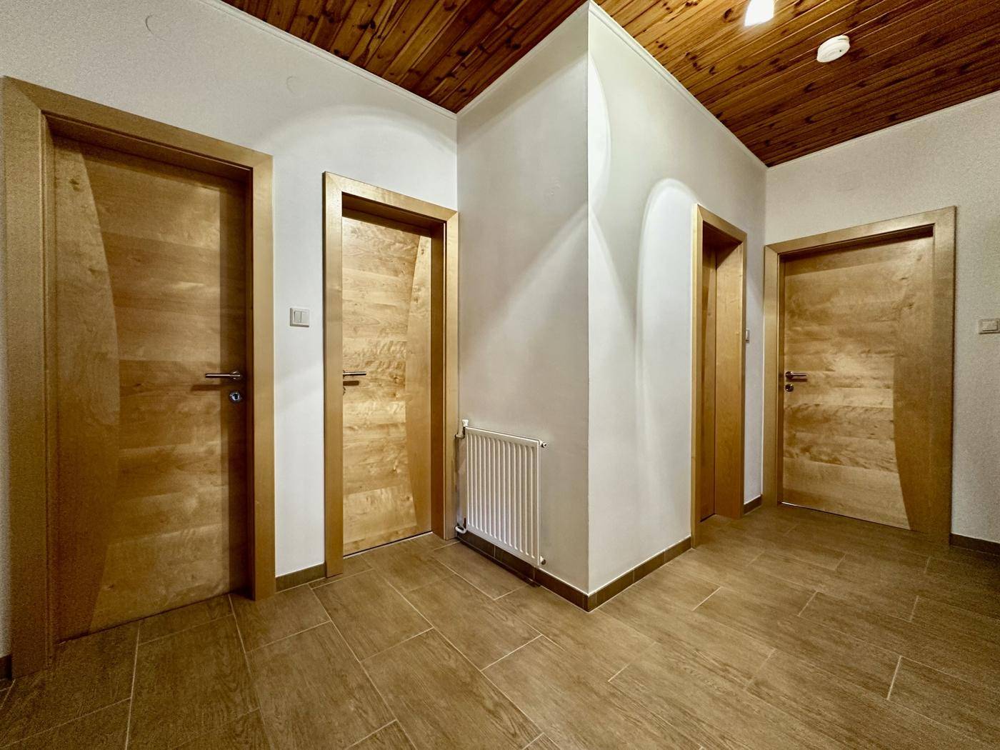 Heller Flur mit Holztüren, Fliesenboden und Holzdeckenverkleidung, gut beleuchtet.