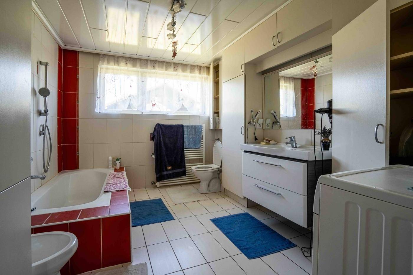 Badezimmer mit Badewanne, Dusche, Waschbecken und Fenster in rotem und weißem Design.