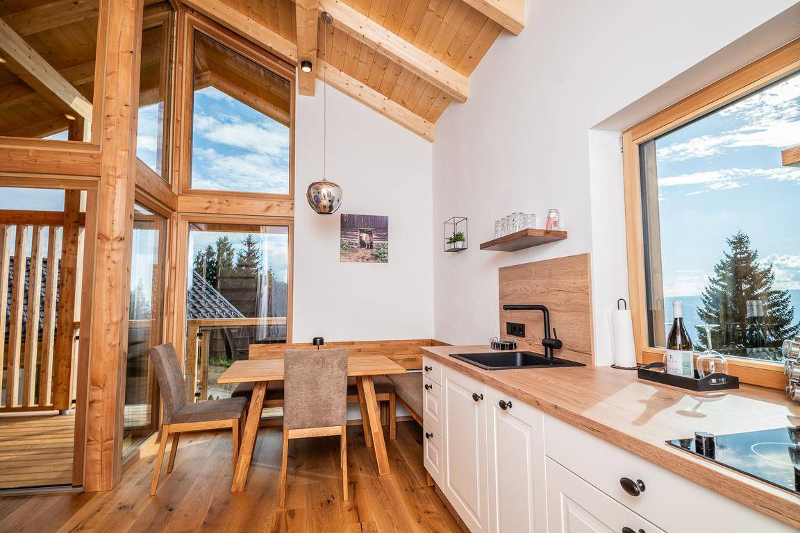 Helle Küche mit Holzelementen, Essbereich und großen Fenstern mit Blick auf die Natur.