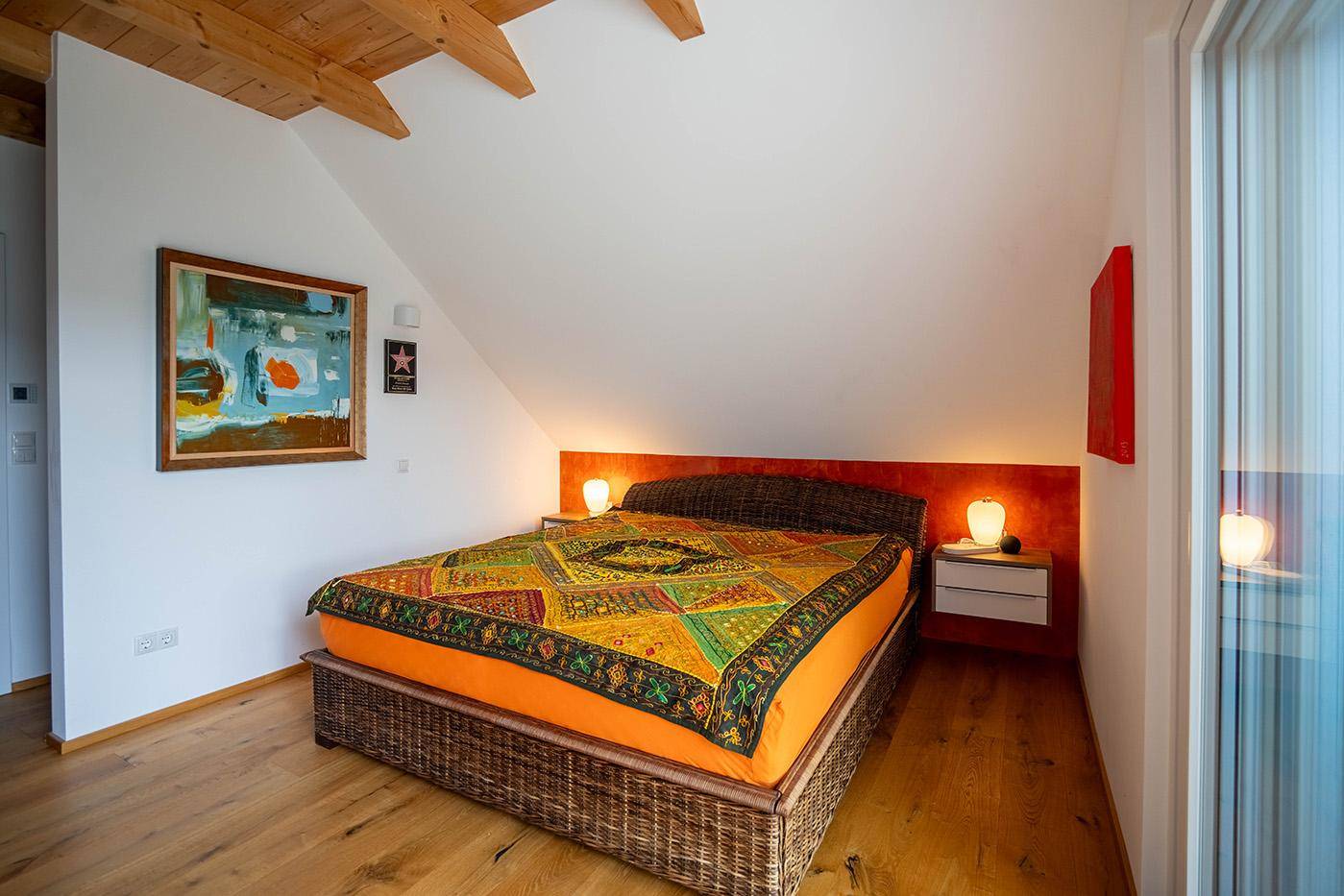 Gemütliches Schlafzimmer im Dachgeschoss mit Holzbalken und farbenfroher Bettwäsche.