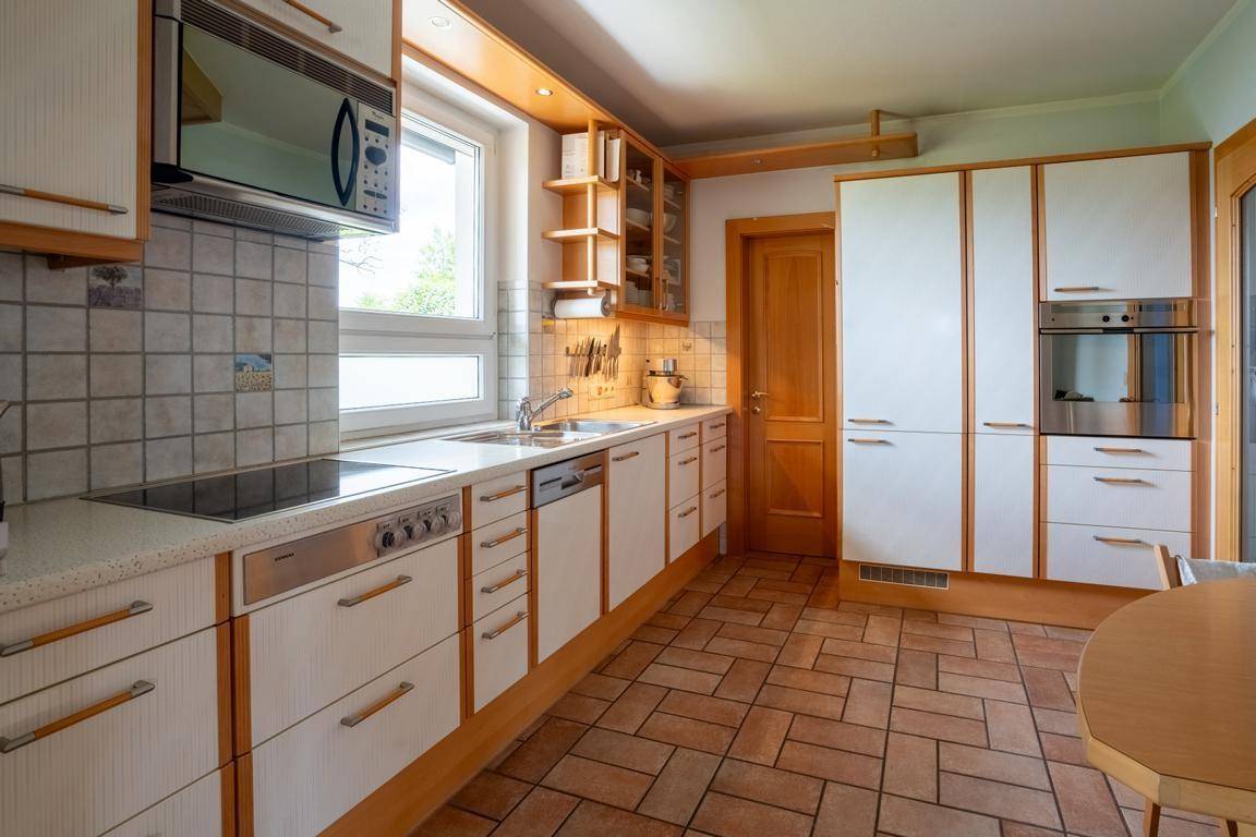Funktionale Küche mit weißen Holzschränken, integrierten Geräten und Terrakottafliesen.