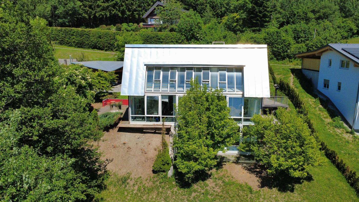 Architektonisch ansprechendes Haus mit großer Glasfront und Metallverkleidung in grüner Umgebung.