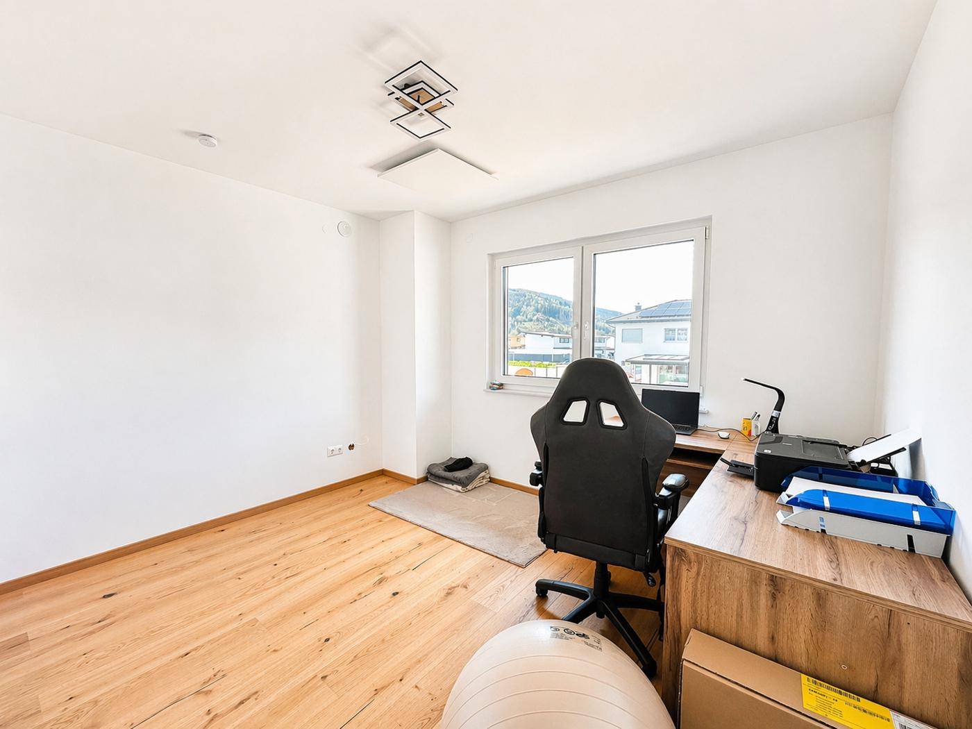 Helles Arbeitszimmer mit Holzboden, Schreibtisch und Blick auf die Umgebung.