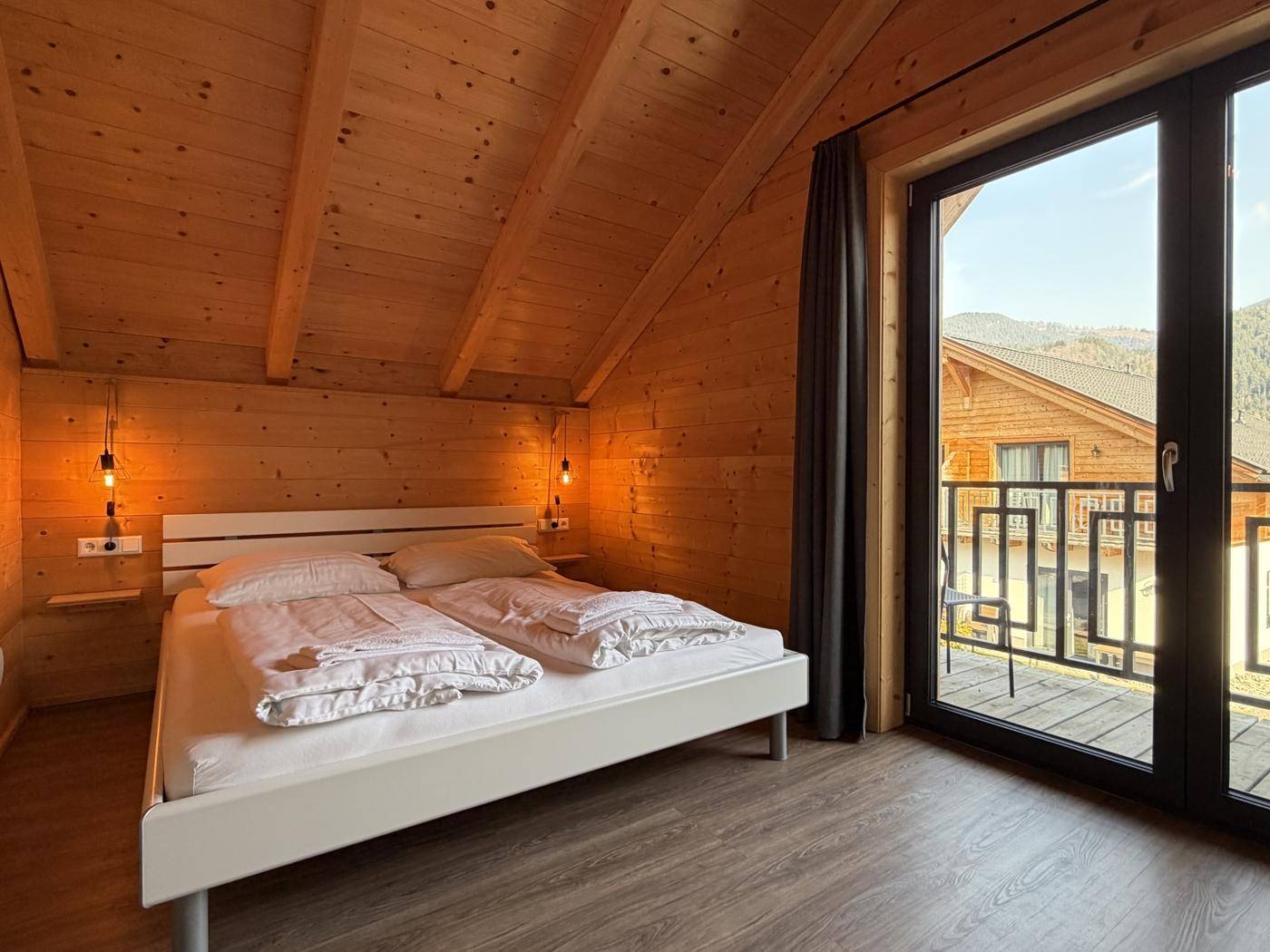 Gemütliches Schlafzimmer mit Holzwänden, Dachschräge und Balkonzugang.