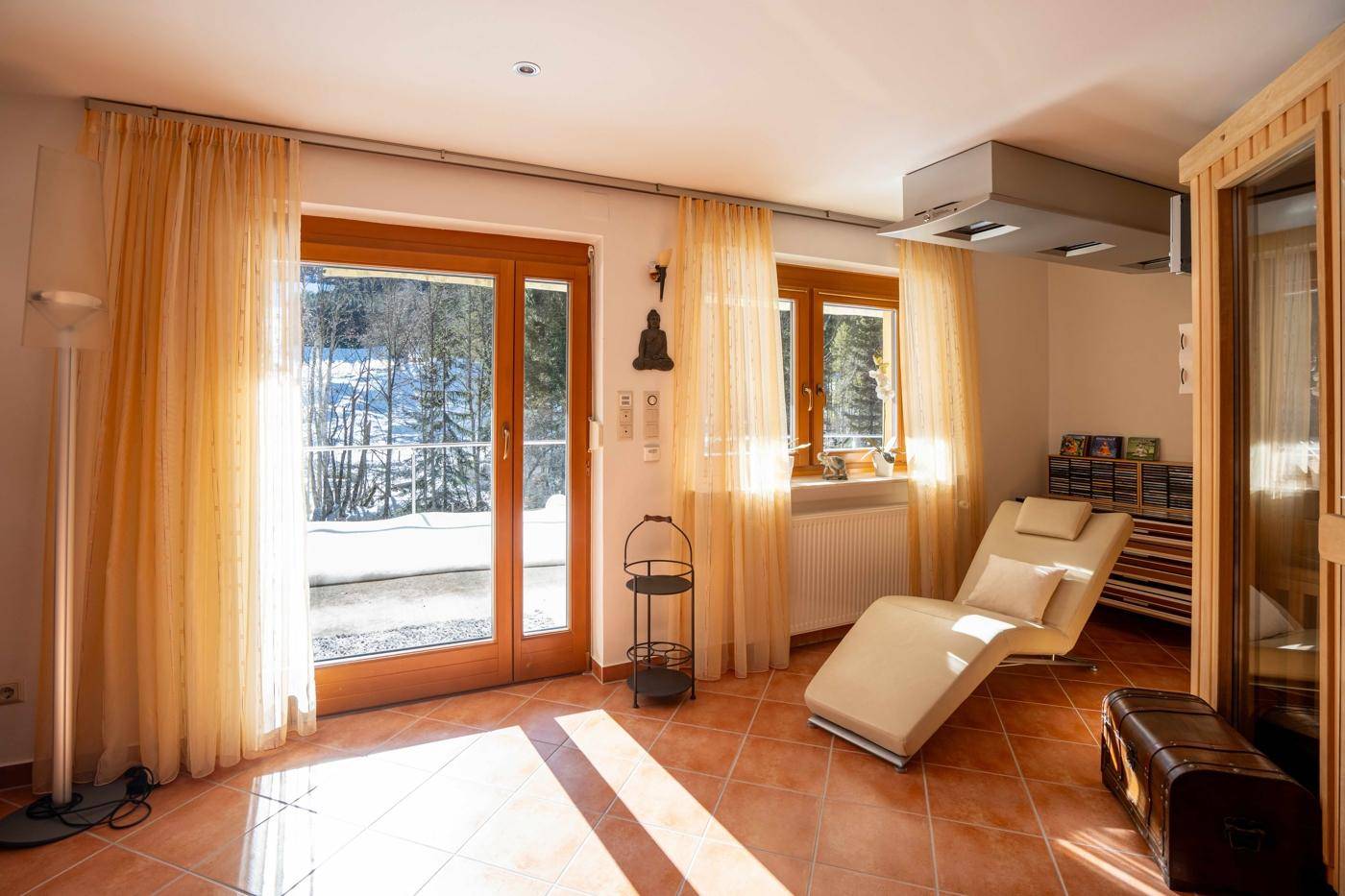 Entspannungsraum mit Liege, großen Fenstern und Zugang nach draußen, ideal für Wellness.