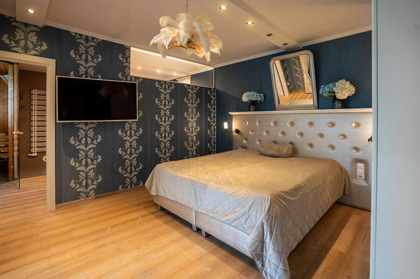 Modernes Schlafzimmer mit blauer Tapete, großem Bett und integriertem Spiegel.