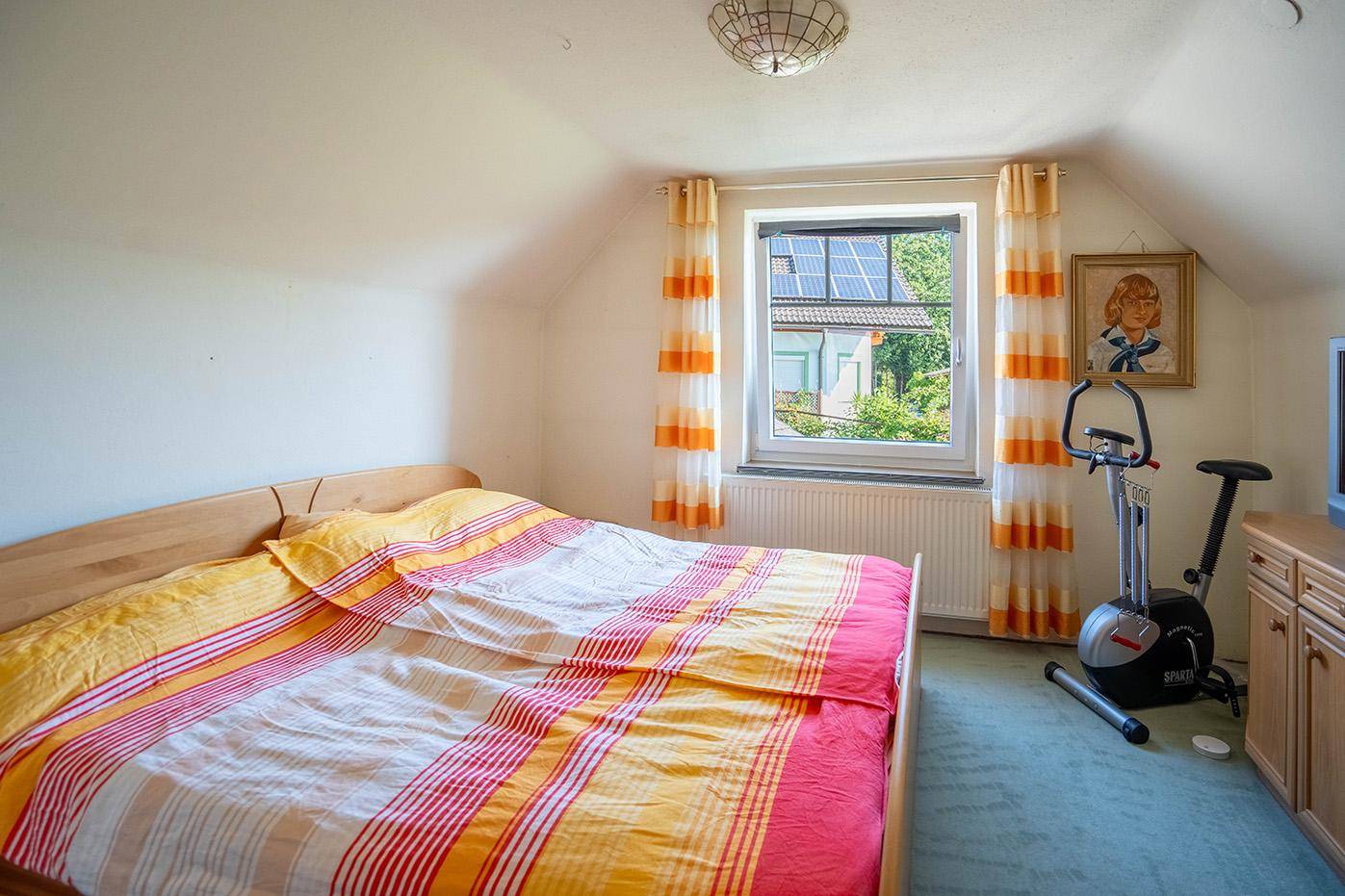 Schlafbereich mit Doppelbett, Fensterblick auf Solaranlagen und einem Heimtrainer für sportliche Aktivitäten.