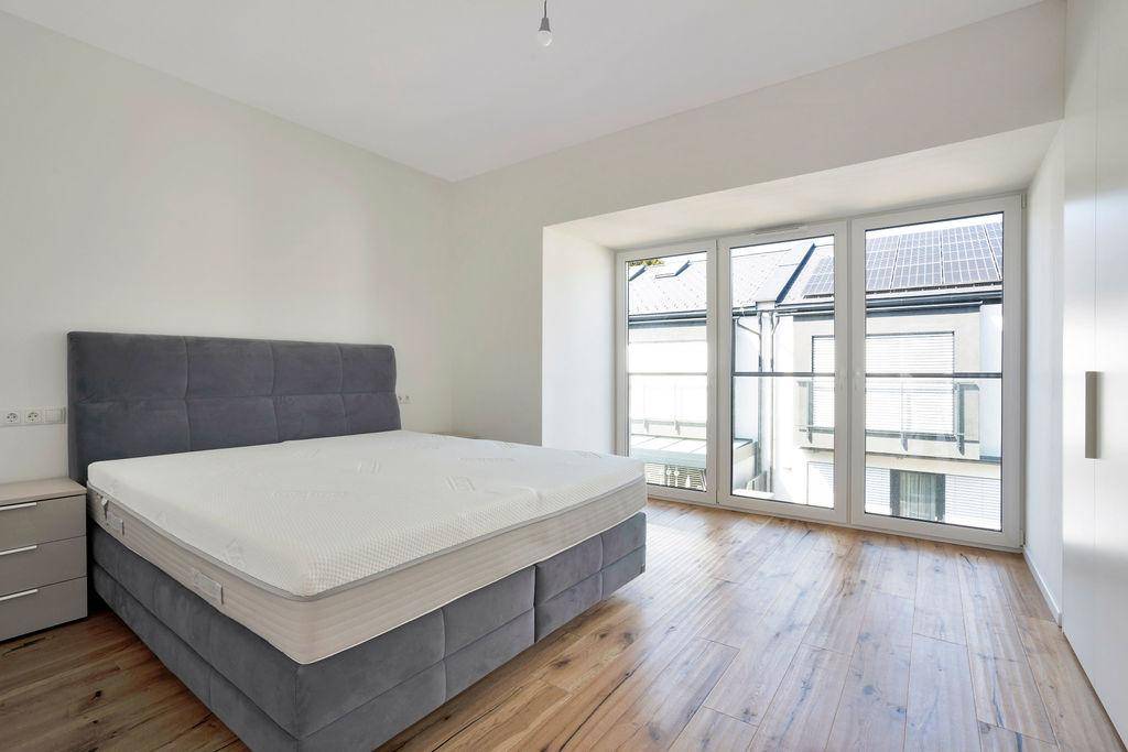 Gemütliches Schlafzimmer mit großem Bett, Nachttisch und viel Tageslicht durch die breiten Fenster.