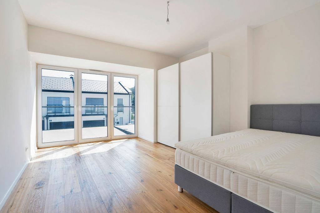 Helles Schlafzimmer mit Holzboden, großem Bett und weißen Einbauschränken, mit Blick auf Nachbargebäude.