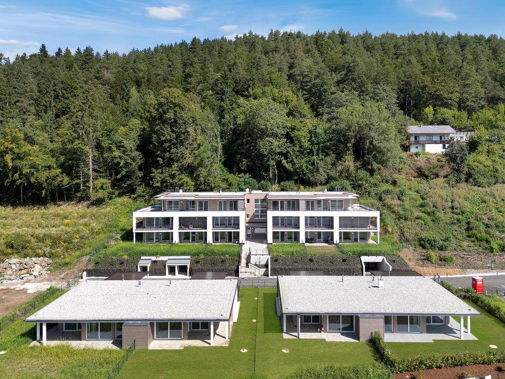 Luftaufnahme der modernen Wohnanlage eingebettet in die bewaldete Hanglandschaft.