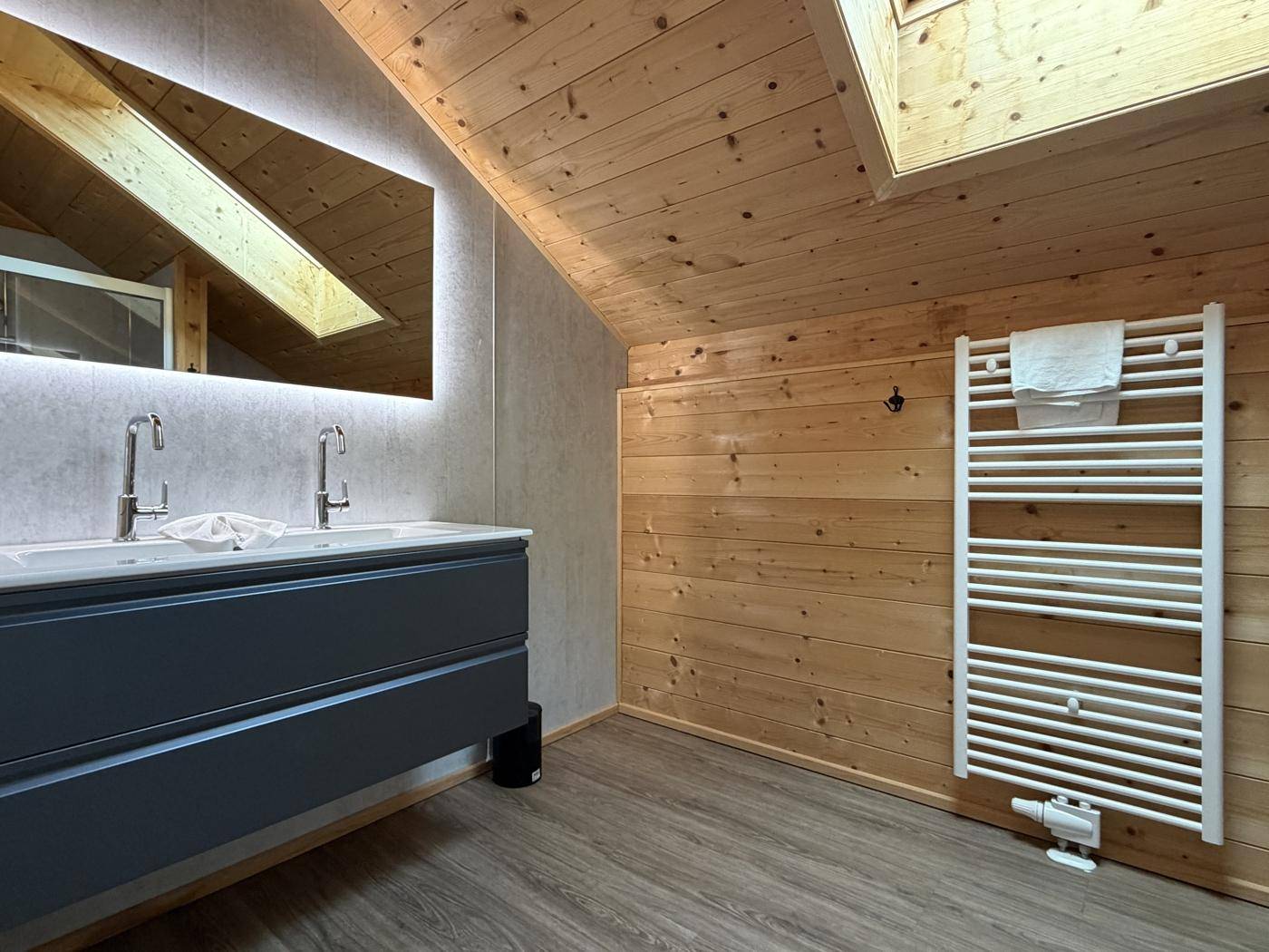 Modernes Badezimmer mit Doppelwaschbecken, beheiztem Handtuchhalter und Dachfenster.
