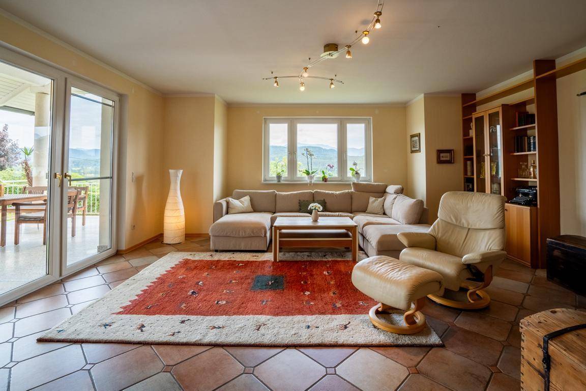 Gemütliches Wohnzimmer mit beiger Eckcouch, Terrakottafliesen und Zugang zur Terrasse mit Bergblick.