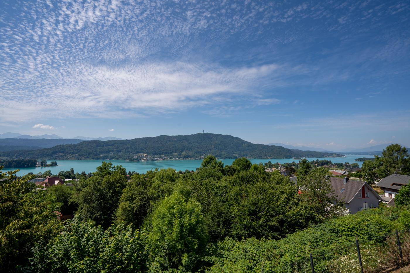 Panoramablick auf den See und die umliegende grüne Landschaft unter blauem Himmel.