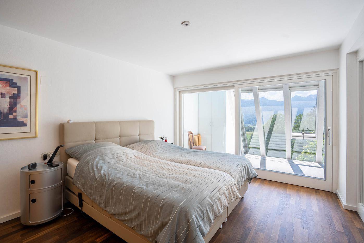 Gemütliches Schlafzimmer mit Doppelbett, Holzboden und großen Fenstern mit Bergblick.