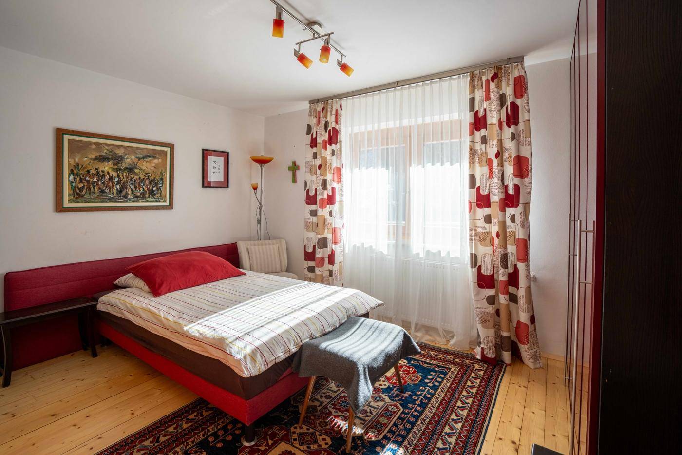 Gemütliches Schlafzimmer mit Holzboden, Teppich und farbenfrohen Vorhängen.